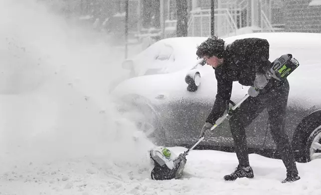 A person clears snow from around a car during a snowstorm in Montreal, Sunday, Feb. 16, 2025. (Graham Hughes/The Canadian Press via AP)