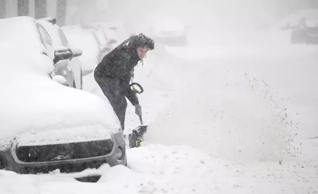 A person clears snow from around a car during a snowstorm in Montreal, Sunday, Feb. 16, 2025. (Graham Hughes/The Canadian Press via AP)