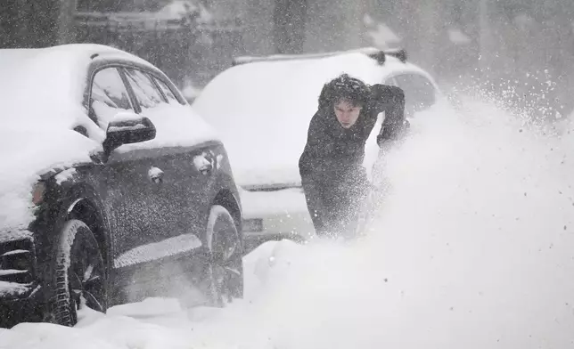 A person clears snow from around a car during a snowstorm in Montreal, Sunday, Feb. 16, 2025. (Graham Hughes/The Canadian Press via AP)