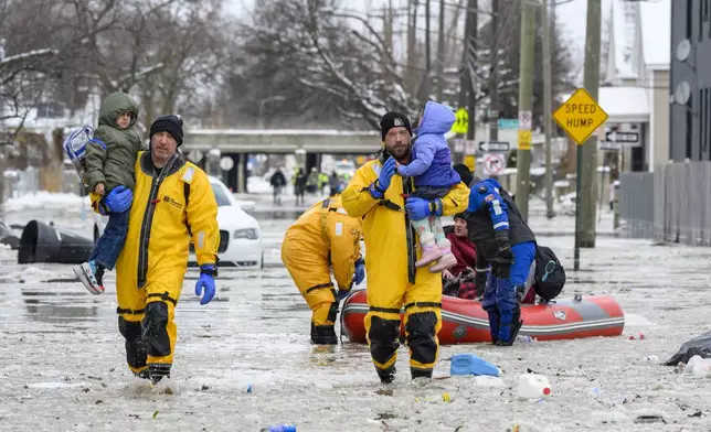 Members of the Downriver Dive Team carry children to safety after a water main break in Detroit caused massive flooding, triggering evacuations, Monday, Feb. 17, 2025. (Andy Morrison/Detroit News via AP)