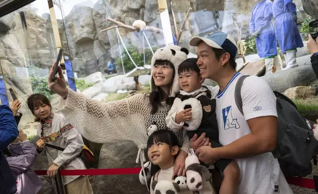 Visitors take selfie at the panda enclosure as the Hong Kong-born giant panda twin cubs make their debut appearance to public in Ocean Park in Hong Kong, Sunday, Feb. 16, 2025. (AP Photo/Chan Long Hei)