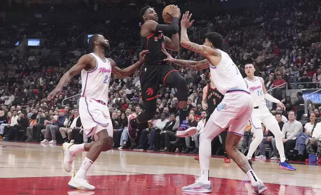 Toronto Raptors' RJ Barrett drives to the net on Miami Heat's Kel'el Ware, right, and Andrew Wiggins, left, during first half NBA basketball action in Toronto on Friday, February 21, 2025. (Chris Young/The Canadian Press via AP)