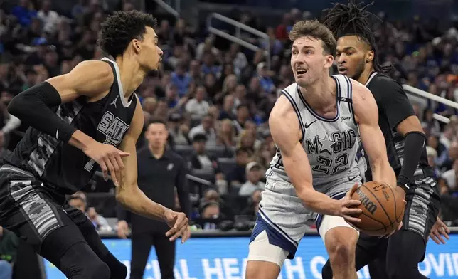 Orlando Magic forward Franz Wagner (22) looks for a shot against San Antonio Spurs center Victor Wembanyama, left, and guard Stephon Castle during the first half of an NBA basketball game Saturday, Feb. 8, 2025, in Orlando, Fla. (AP Photo/John Raoux)