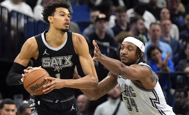 San Antonio Spurs center Victor Wembanyama, left, passes the ball around Orlando Magic center Wendell Carter Jr. (34) during the first half of an NBA basketball game Saturday, Feb. 8, 2025, in Orlando, Fla. (AP Photo/John Raoux)