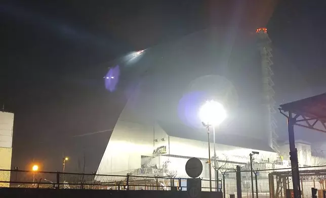 In this photo provided by the Ukrainian Emergency Service, a searchlight illuminates a hole in the roof of a damaged sarcophagus, that covers the destroyed 4th reactor of Chernobyl nuclear power plant, following a Russian drone attack in Chernobyl, Ukraine, Friday, Feb. 14, 2025. (Ukrainian Emergency Service via AP)