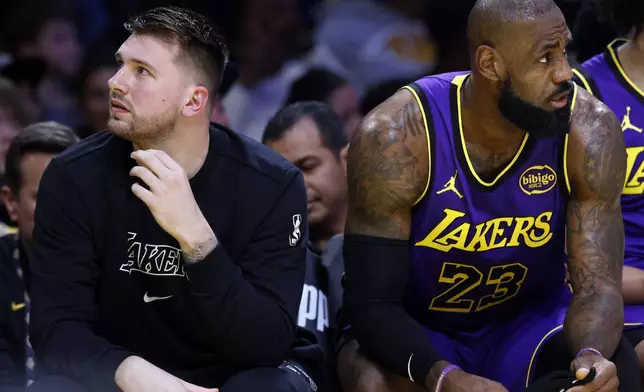 Los Angeles Lakers guard Luka Doncic, left, and forward LeBron James (23) look on from the bench during the first half of an NBA basketball game against the Golden State Warriors, Thursday, Feb. 6, 2025, in Los Angeles. (AP Photo/Kevork Djansezian)