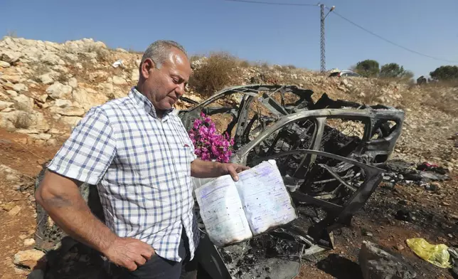 Samir Ayoub, whose sister, Samira Ayoub, and her three granddaughters, Rimas, 14; Taline, 12, and Liane, 10, were killed by an Israeli airstrike, holds one of their burned school books next to their vehicle's remains in the town of Ainata, southern Lebanon, near the border with Israel, on Monday, Nov. 6, 2023. (AP Photo/Mohammed Zaatari)