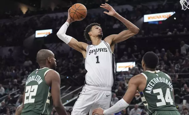 San Antonio Spurs center Victor Wembanyama (1) drives to the basket against Milwaukee Bucks forwards Khris Middleton (22) and Giannis Antetokounmpo (34) during the second half of an NBA basketball game in San Antonio, Friday, Jan. 31, 2025. (AP Photo/Eric Gay)