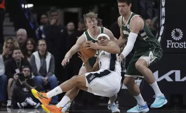 San Antonio Spurs forward Keldon Johnson, front, is fouled as he drives to the basket against Milwaukee Bucks guard AJ Green, left, and Milwaukee Bucks center Brook Lopez, right, during the first half of an NBA basketball game in San Antonio, Friday, Jan. 31, 2025. (AP Photo/Eric Gay)