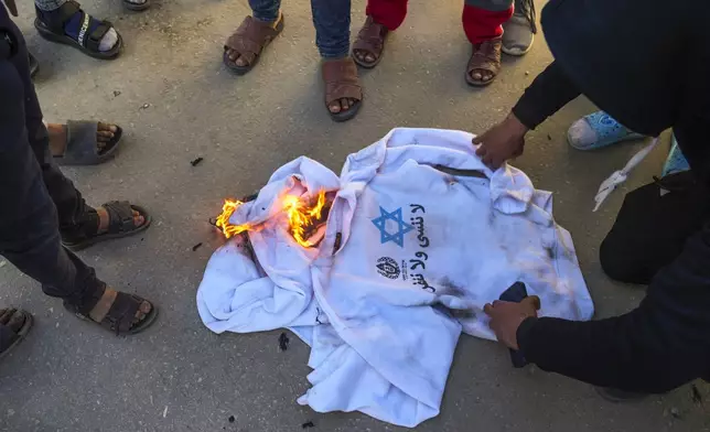 A crowd burns the shirts worn by freed Palestinian prisoners in Khan Younis, Gaza Strip, Saturday, Feb. 15, 2025, as they arrive in Gaza after being released from an Israeli prison following a ceasefire agreement between Hamas and Israel. (AP Photo/Abdel Kareem Hana)