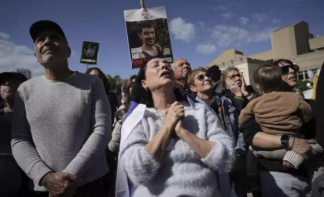 People holding posters with photos of Israelis hostages Eli Sharabi, Or Levy and Ohad Ben Ami, react at the so-called "hostages square" as they watch their release live on a television screen in Tel Aviv, Israel on Saturday, Feb. 8, 2025. (AP Photo/Oded Balilty)
