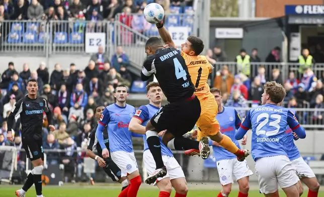 Kiel goalkeeper Timon Weiner, right, reaches for the ball past Leverkusen's Jonathan Tah during the Bundesliga soccer match between Holstein Kiel and Bayer Leverkusen at Holstein-Stadion, Kiel, Germany, Saturday Feb. 22, 2025. (Gregor Fischer/dpa via AP)