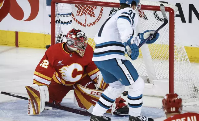 San Jose Sharks' Macklin Celebrini, top right, scores against Calgary Flames goalie Dustin Wolf, left, during first-period NHL hockey game action in Calgary, Alberta, Sunday, Feb. 23, 2025. (Jeff McIntosh/The Canadian Press via AP)