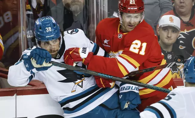 San Jose Sharks' Mario Ferraro, left, is checked by Calgary Flames' Kevin Rooney (21) during first-period NHL hockey game action in Calgary, Alberta, Sunday, Feb. 23, 2025. (Jeff McIntosh/The Canadian Press via AP)