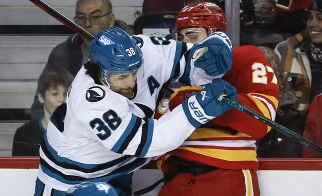 San Jose Sharks' Mario Ferraro, left, checks Calgary Flames' Matthew Coronato, right, during first-period NHL hockey game action in Calgary, Alberta, Sunday, Feb. 23, 2025. (Jeff McIntosh/The Canadian Press via AP)