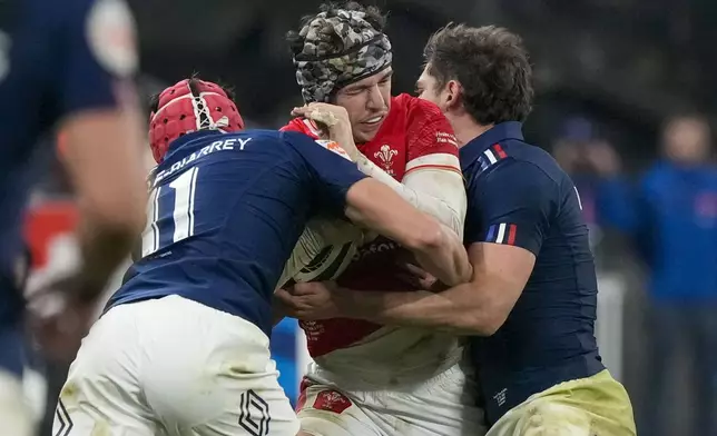 Wales' Tom Rogers, center, is tackled by France's Louis Bielle-Biarrey, left, during the Six Nations rugby union match between France and Wales at the Stade de France in Saint-Denis, outside Paris, Friday, Jan. 31, 2025. (AP Photo/Michel Euler)