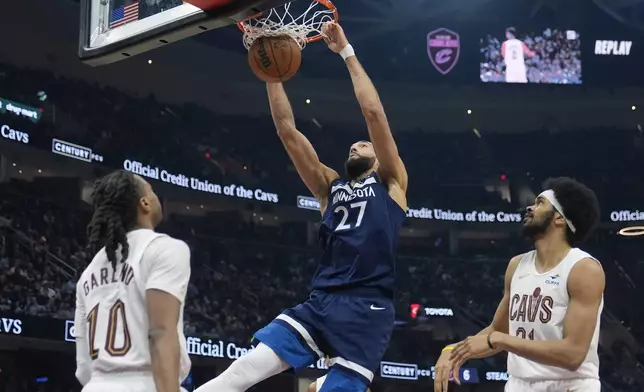 Minnesota Timberwolves center Rudy Gobert (27) dunks between Cleveland Cavaliers guard Darius Garland (10) and center Jarrett Allen, right, in the first half of an NBA basketball game Monday, Feb. 10, 2025, in Cleveland. (AP Photo/Sue Ogrocki)