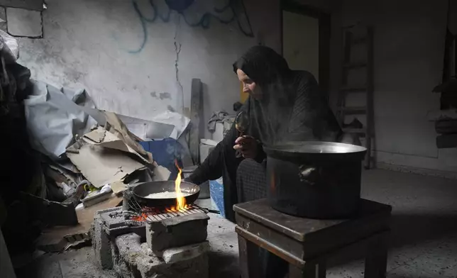Khadra Abu Libda, 59, burns wood to cook food inside a room in the Jabaliya refugee camp in the northern Gaza Strip, Sunday, Feb. 9, 2025. The family didn’t know who spray painted "Hamas" on the wall, or whether the house was used by fighters during the battles. (AP Photo/Abdel Kareem Hana)