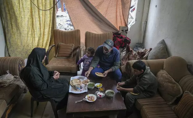 Khalid Nassar, 61, sits with his wife, Khadra Abu Libda, 59, and his grandchildren for lunch, with fabric covering the hole in a wall of their destroyed house in the Jabaliya refugee camp in the northern Gaza Strip, Sunday, Feb. 9, 2025. (AP Photo/Abdel Kareem Hana)