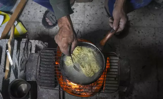 Khalid Nassar uses an open fire to cook noodles for his grandchildren inside his damaged house in the Jabaliya refugee camp in the northern Gaza Strip, Sunday, Feb. 9, 2025. (AP Photo/Abdel Kareem Hana)