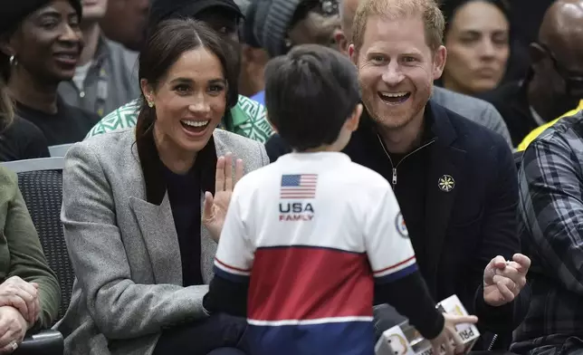 Britain's Prince Harry speaks with a young boy who brought a toy figurine of his likeness for him to autograph, as he and his wife Meghan, the Duke and Duchess of Sussex, watch the U.S. and Nigeria play a wheelchair basketball game during the 2025 Invictus Games, in Vancouver, British Columbia, Sunday, Feb. 9, 2025. (Darryl Dyck/The Canadian Press via AP)