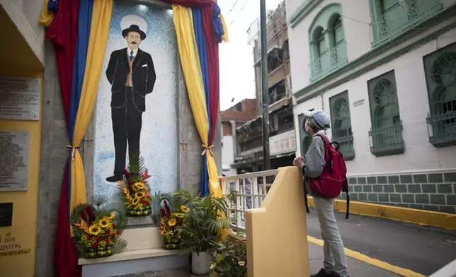 FILE - A woman prays at a memorial dedicated to Dr. Jose Gregorio Hernandez, on the street where he died when hit by a car in 1919, in La Pastora neighborhood of Caracas, Venezuela, April 28, 2021. (AP Photo/Ariana Cubillos, File)