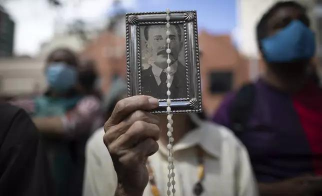 FILE - A devotee holds up a framed image of of Dr. Jose Gregorio Hernández, outside La Candelaria church where he is buried, in Caracas, Venezuela, Oct. 26, 2020. The remains of Hernández, popularly known as the "doctor of the poor", were exhumed in a private ceremony inside the church as part of a Vatican request for his beatification process. (AP Photo/Ariana Cubillos, File)