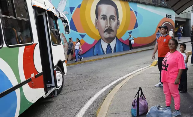 Commuters wait for transport next to a mural depicting Dr. Jose Gregorio Hernandez in La Pastora neighborhood of Caracas, Venezuela, after Pope Francis approved the canonization of the physician as Venezuela's first saint on Tuesday, Feb. 25, 2025. (AP Photo/Cristian Hernandez)