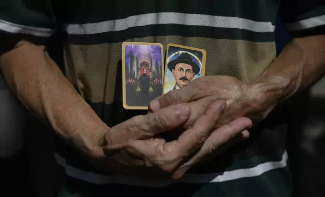 FILE - A man holds prayer cards with images of Dr. Jose Gregorio Hernandez on the day of his beatification ceremony outside the church that guards his remains in La Candelaria neighborhood of Caracas, Venezuela, April 30, 2021. (AP Photo/Matias Delacroix, File)