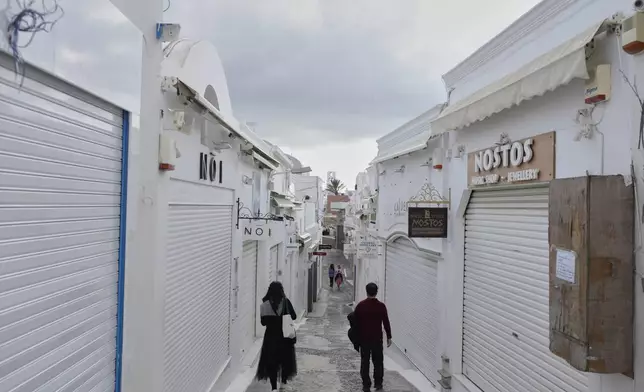 Tourists pass by closed shops in Fira town as Greek authorities are taking emergency measures in response to intense seismic activity on the popular Aegean Sea holiday island of Santorini, southern Greece, Monday, Feb. 3, 2025. (AP Photo/Petros Giannakouris)