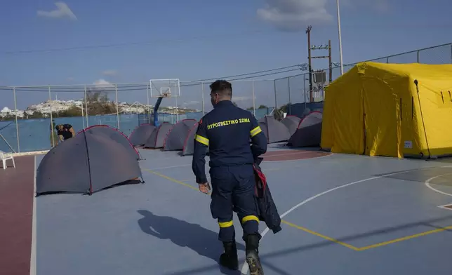 A firefighter walks next to tents set up at a basketball court to accommodate Fire Service rescuers as Greek authorities is taking emergency measures in response to intense seismic activity on the popular Aegean Sea holiday island of Santorini, southern Greece, Monday, Feb. 3, 2025. (AP Photo/Petros Giannakouris)