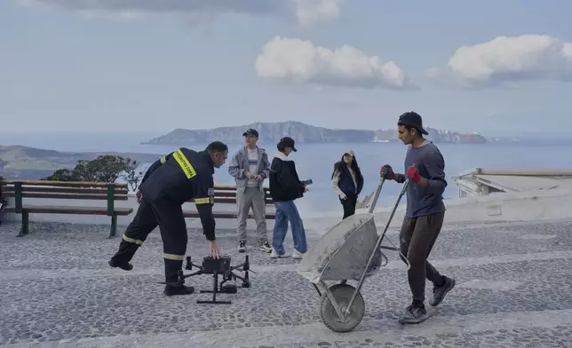 A firefighter controls a drone next to tourists after emergency crews were deployed to the island as Greek authorities are taking emergency measures in response to intense seismic activity on the popular Aegean Sea holiday island of Santorini, southern Greece, Monday, Feb. 3, 2025. (AP Photo/Petros Giannakouris)