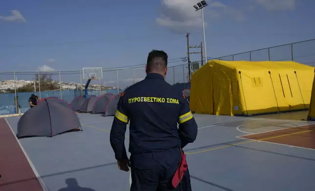 A firefighter walks next to tents set up at a basketball court to accommodate Fire Service rescuers as Greek authorities is taking emergency measures in response to intense seismic activity on the popular Aegean Sea holiday island of Santorini, southern Greece, Monday, Feb. 3, 2025. (AP Photo/Petros Giannakouris)