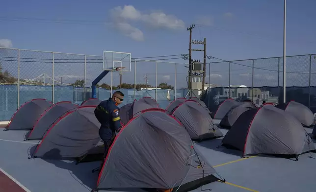 A firefighter walks among tents set up at a basketball court to accommodate Fire Service rescuers as Greek authorities are taking emergency measures in response to intense seismic activity on the popular Aegean Sea holiday island of Santorini, southern Greece, Monday, Feb. 3, 2025. (AP Photo/Petros Giannakouris)