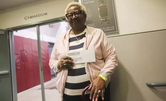 Impacted by the Eaton Fire, Katherine Anderson poses with an envelope containing a check as she leaves the gymnasium of Pasadena City College where The Change Reaction is handing out about 1,000 checks of between $2,500-$5,000 to people impacted by the wildfire, Tuesday, Jan. 28, 2025 in Pasadena, Calif. (AP Photo/Etienne Laurent)
