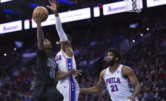 Brooklyn Nets' Keon Johnson, left, goes up for a shot against Philadelphia 76ers' Paul George, center, and Joel Embiid during the first half of an NBA basketball game, Saturday, Feb. 22, 2025, in Philadelphia. (AP Photo/Matt Slocum)