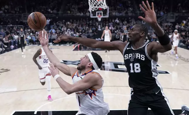 Phoenix Suns guard Devin Booker (1) is defended by San Antonio Spurs center Bismack Biyombo (18) as he tries to score during the second half of an NBA basketball game in Austin, Texas, Thursday, Feb. 20, 2025. (AP Photo/Eric Gay)