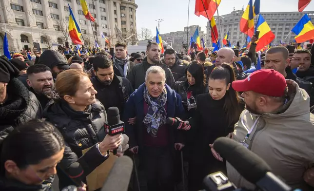 Calin Georgescu, the winner of Romania's first round of presidential election, annulled by the Constitutional Court, uses crutches walking between supporters gathered for a protest outside the Romanian parliament in Bucharest, Romania, Saturday, Feb. 22, 2025. (AP Photo/Alexandru Dobre)