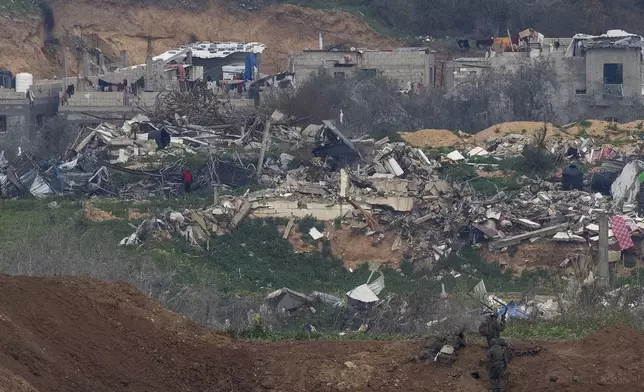 A Palestinian man wearing a red shirt, left, stands amidst the rubble of destroyed buildings, watching Israeli soldiers, bottom right, take position in the northern Gaza Strip, as seen from southern Israel, Sunday, Feb. 9, 2025. (AP Photo/Ohad Zwigenberg)