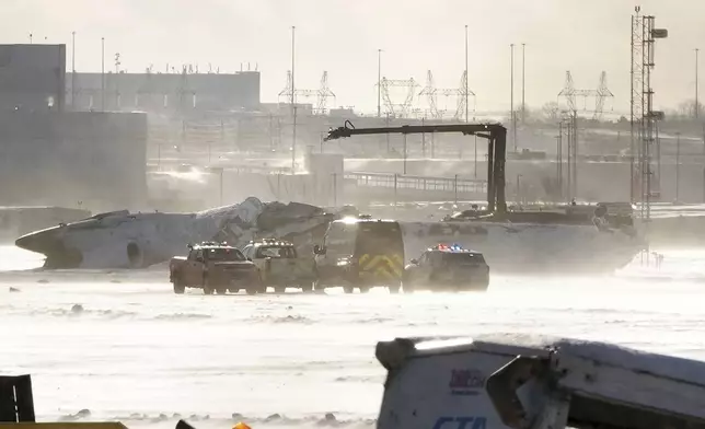 Emergency response vehicles are seen nearby an upside down Delta Air Lines plane, which was heading from Minneapolis to Toronto when it crashed on the runway at Pearson International Airport, in Toronto, Monday, Feb. 17, 2025. (Teresa Barbieri/The Canadian Press via AP)