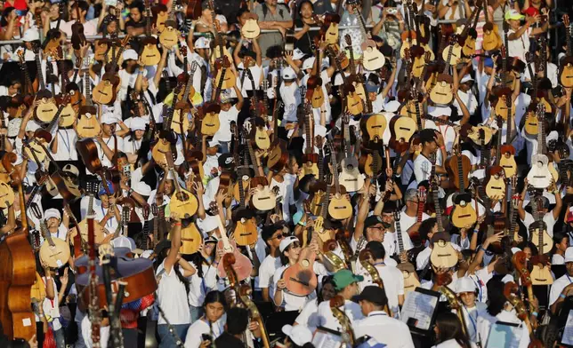 Youth raise their instruments during a concert celebrating the 50th anniversary of Venezuela's national system of children and youth orchestras in Caracas, Venezuela, Sunday, Feb. 23, 2025. (AP Photo/Cristian Hernandez)