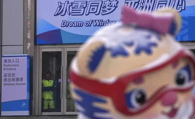 A worker stands watch at an entrance door of the venue for the opening ceremony of the Asian Winter Games in Harbin, China's Heilongjiang province on Friday, Feb. 7, 2025. (AP Photo/Andy Wong)