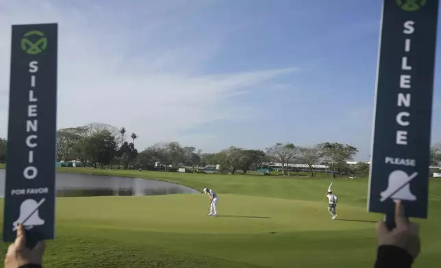 "Silence" signs are held up as Kaito Onishi, of Japan, watches his putt on the green of the first hole during the second round of the Mexico Open golf tournament in Puerto Vallarta, Mexico, Friday, Feb. 21, 2025. (AP Photo/Fernando Llano)