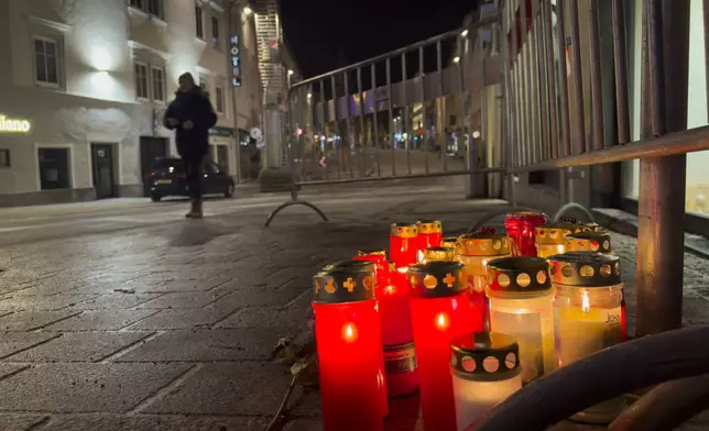A pedestrian walk past candles at the site of a stabbing attack in Villach, Austria, Sunday, Feb. 16, 2025. (AP Photo/Darko Bandic)