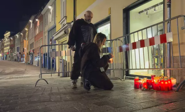 A person lights a candle at the site of a stabbing attack in Villach, Austria, Sunday, Feb. 16, 2025. (AP Photo/Darko Bandic)
