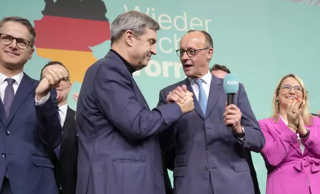 Friedrich Merz, with the microphone, the candidate of the mainstream conservative Christian Democratic Union party, shakes hands with Markus Soeder, leader of CSU and Minister-President of Bavaria, at the party headquarters in Berlin, Germany, Sunday, Feb. 23, 2025, after the German national election. (AP Photo/Markus Schreiber)