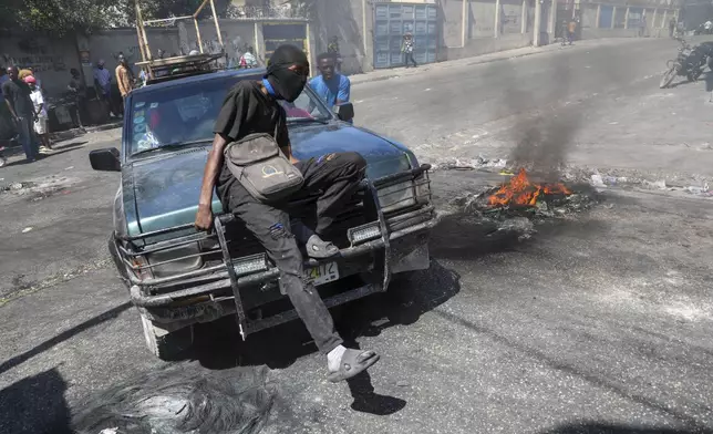 A protester sits on the hood of a car during a demonstration to demand government action against gang violence in Port-au-Prince, Haiti, Thursday, Feb. 20, 2025. (AP Photo/Odelyn Joseph)