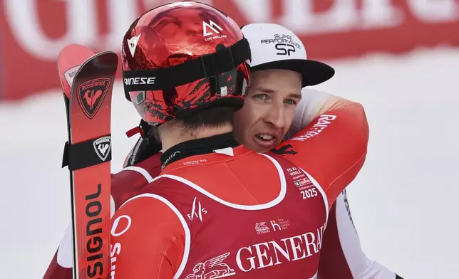 Switzerland's Loic Meillard, back to camera, hugs Austria's Raphael Haaser after he won the gold medal in a men's giant slalom, at the Alpine Ski World Championships, in Saalbach-Hinterglemm, Austria, Friday, Feb. 14, 2025. (AP Photo/Marco Trovati)