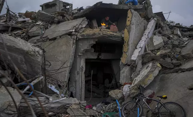 Mohammad Naser, sits by a fire as he takes cover from the rain under the destruction of his house caused by the Israeli air and ground offensive in Jabaliya, Gaza Strip, Thursday, Feb. 6, 2025. (AP Photo/Abdel Kareem Hana)