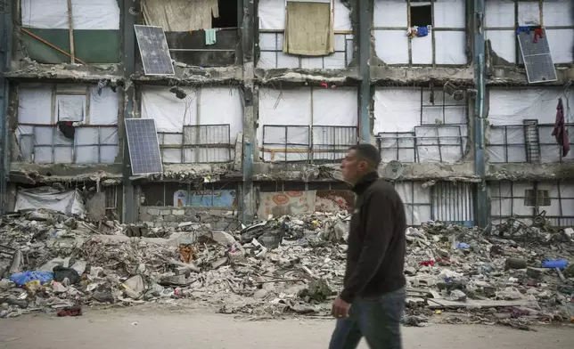A man walks past a house that remains partly standing, but with sheets serving as makeshift walls and solar panels partly working, in an area largely destroyed by the Israeli army's air and ground offensive in Gaza City, Wednesday, Feb. 5, 2025. (AP Photo/Abdel Kareem Hana)